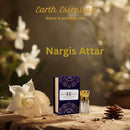 Nargis Attar bottle with packaging and white flowers on a wooden surface, featuring 'Earth Essentials' branding.