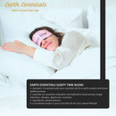 Person sleeping with a pink 'Earth Essentials' sleep mask on, surrounded by white bedding.
